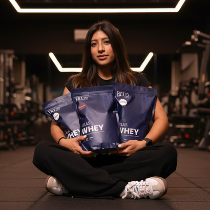 Person holding ATLAS WHEY protein powder packages in a gym setting